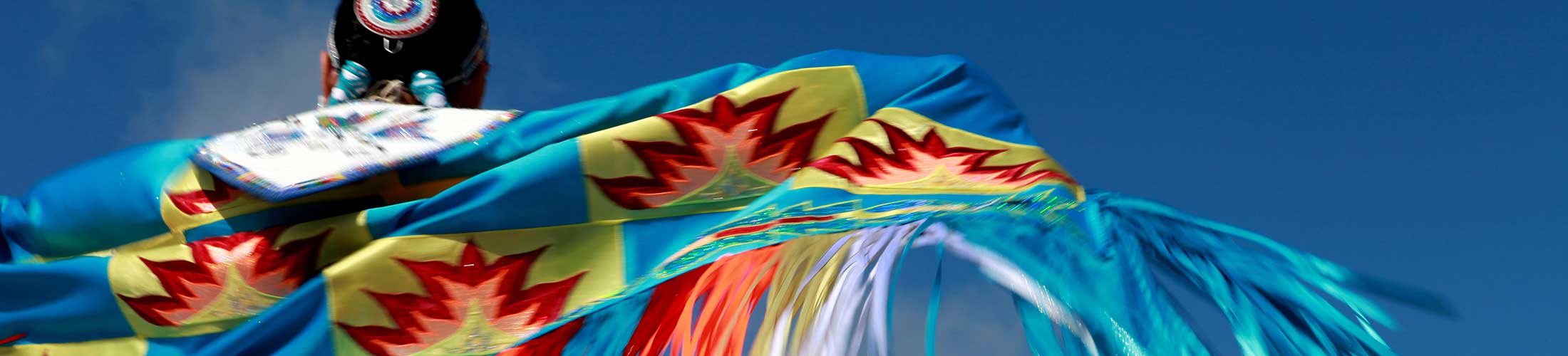 Native American in colorful native apparel with sky in background.