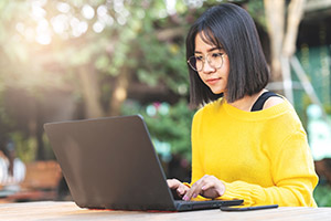 Female student working on laptop outside.