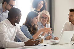 Woman talking sitting in front of laptop with people sitting next to her and standing behind her.