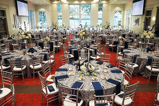 Beautiful tables and chairs with silver and blue decor and flowers set up in the ballroom.