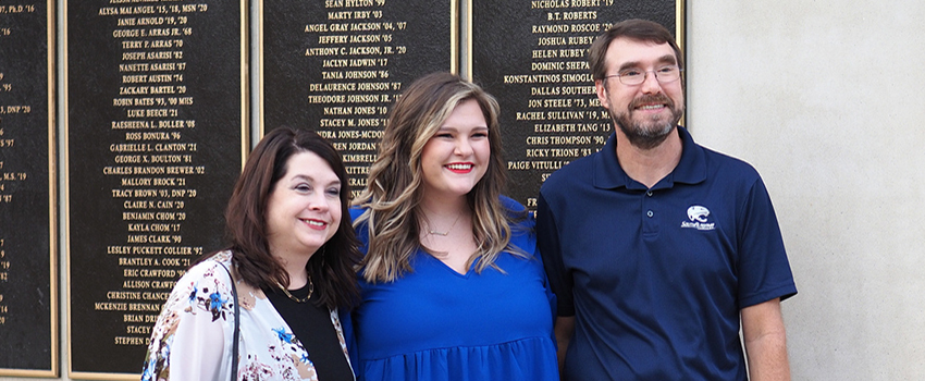 Three alumni in front of Alumni Wall of Donors.