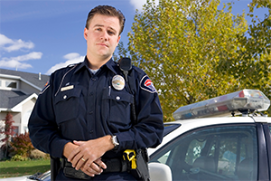 Police officer outside in front of police car.