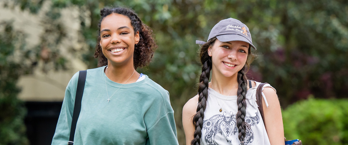 Two female students walking outside on campus smiling.