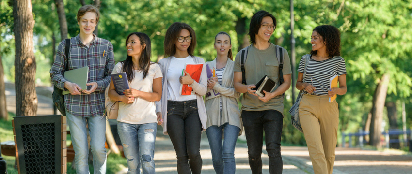 Students walking and talking carrying books outside 