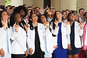 Students during their whitecoat ceremony holding up J sign.