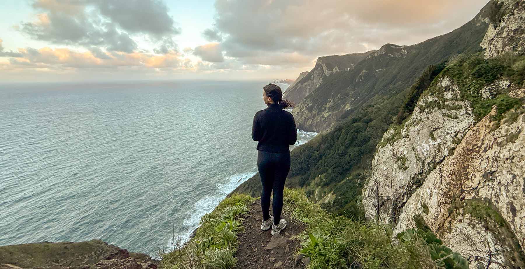 Abby Russ standing beside mountain looking out into the ocean.